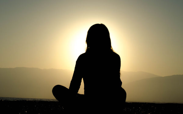 A woman seated cross-legged on a mountain top watching the sunrise