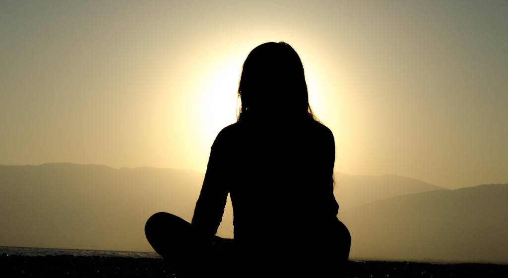 A woman seated cross-legged on a mountain top watching the sunrise