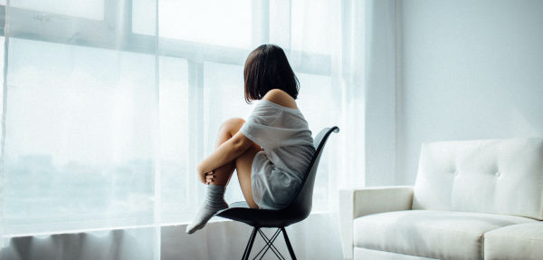 Side profile of a woman seated, holding her legs and looking out the window